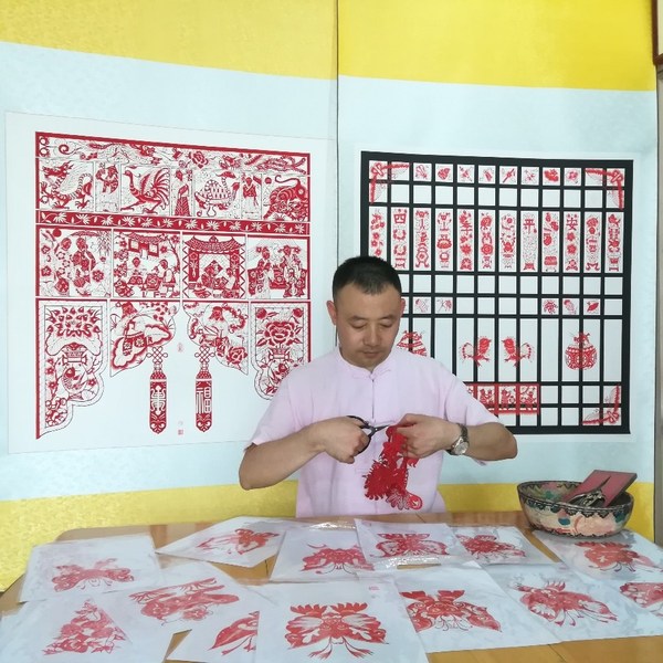 Li Jinbo, a city-level representative inheritor of the national intangible cultural heritage project of Gaomi paper-cutting is creating paper-cutting works featuring a hundred of different dragons.