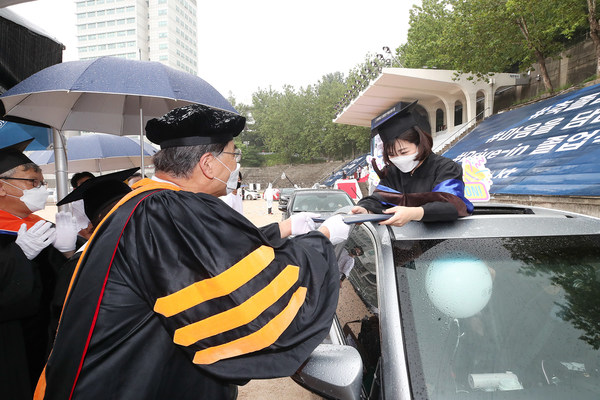 A 2019 graduate who couldn’t have a traditional celebration because of the ongoing COVID-19 pandemic is receiving her diploma in car during the drive-in ceremony held at Hongik University’ Seoul campus, which is supported by KT Corp., on August 21.