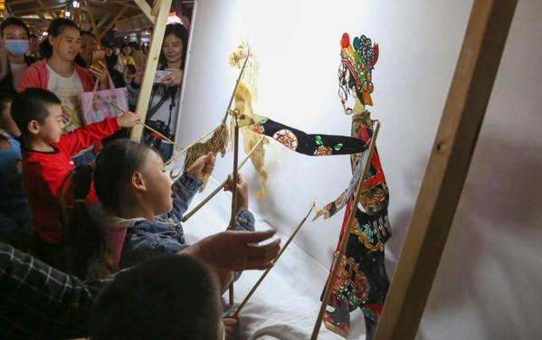 Children are experiencing shadow puppetry at the intangible cultural heritage fair in North Street, Xiangyang, Hubei Province.