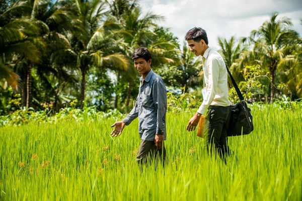 一名小额贷款机构工作人员在柬埔寨田间与一名农民交谈