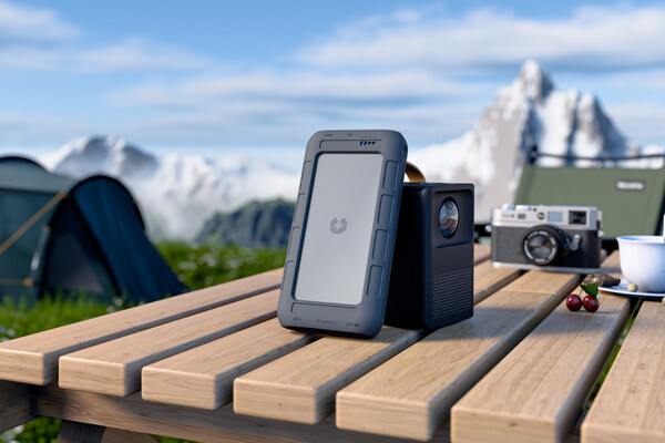 A portable NAS (UT2) leaning against a projector on an outdoor camping table, along with a camera.